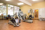 Well-lit interior exercise room with cardio machines, weight equipment, and large windows.