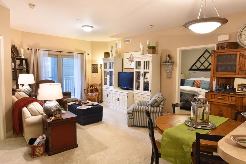 Open-plan living and dining room with a sofa and armchairs around a TV cabinet and a round dining table in the foreground.