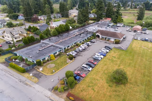 Aerial view of Mountain View Rehabilitation and Care Center showing a single-story building with a flat roof, a parking lot with several cars, surrounding greenery, and nearby residential houses.