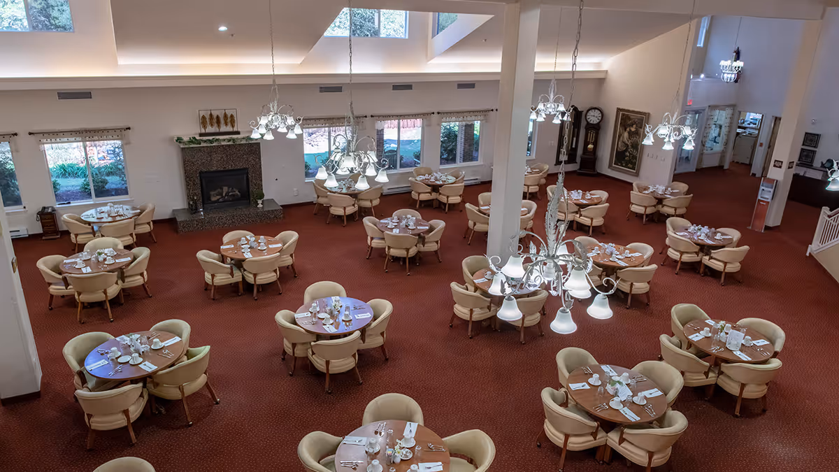 Large dining room with multiple round tables set for meals, chandeliers, and a fireplace.