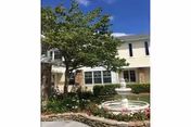 Front courtyard with a white tiered fountain, flower beds, a small tree, and the building facade behind it.