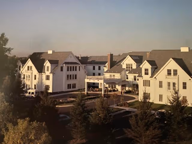 Exterior view of a white multi-wing senior living building with a covered entrance, circular driveway and trees in the foreground.