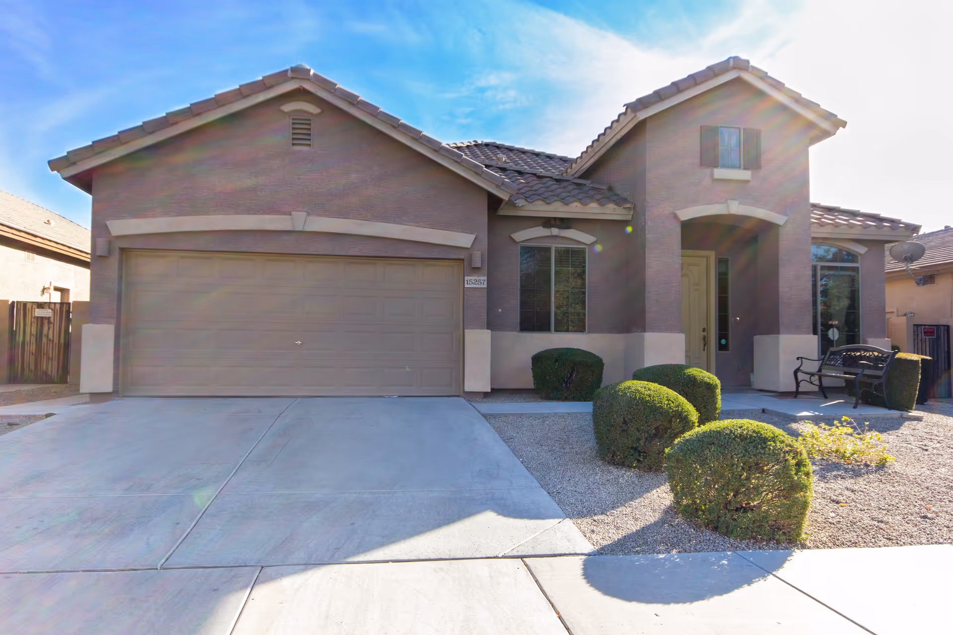 Front exterior of a stucco house with a two-car garage, driveway, and neatly trimmed shrubs.
