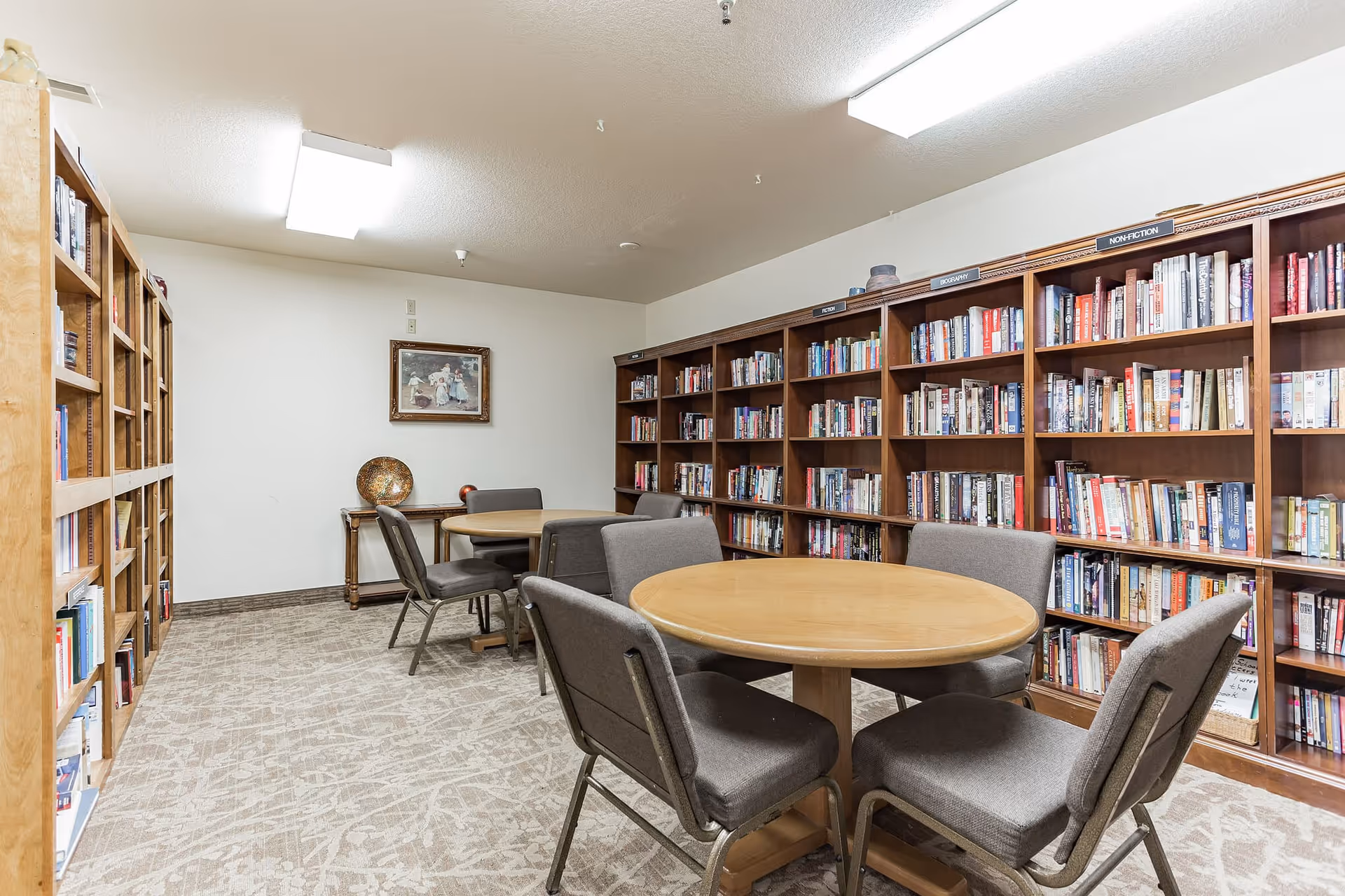 A small library/reading room with bookshelves lining the walls, round tables, and upholstered chairs.