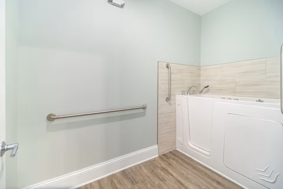 Accessible bathroom with a white walk-in bathtub, stainless grab bars, and wood-look flooring.