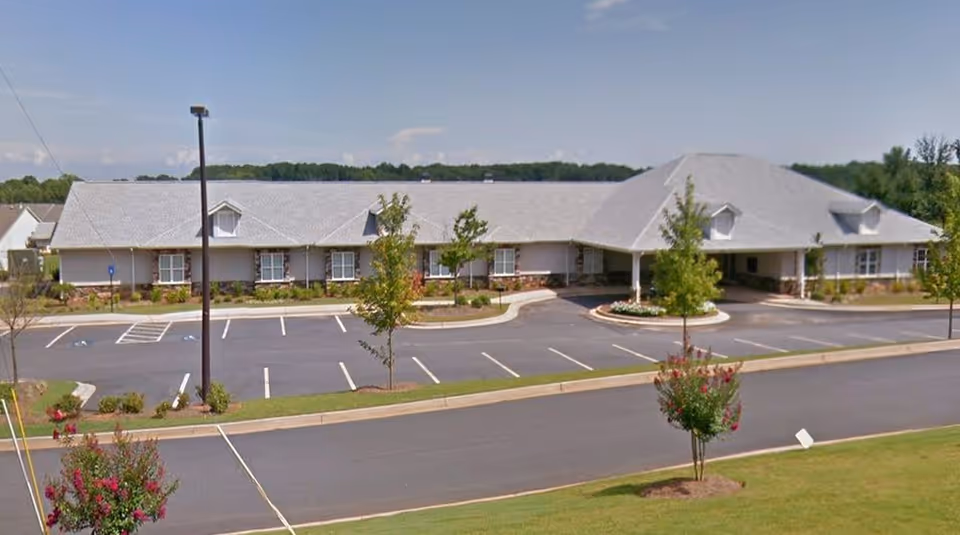Wide view of a single-story memory care facility with a parking lot and landscaping.
