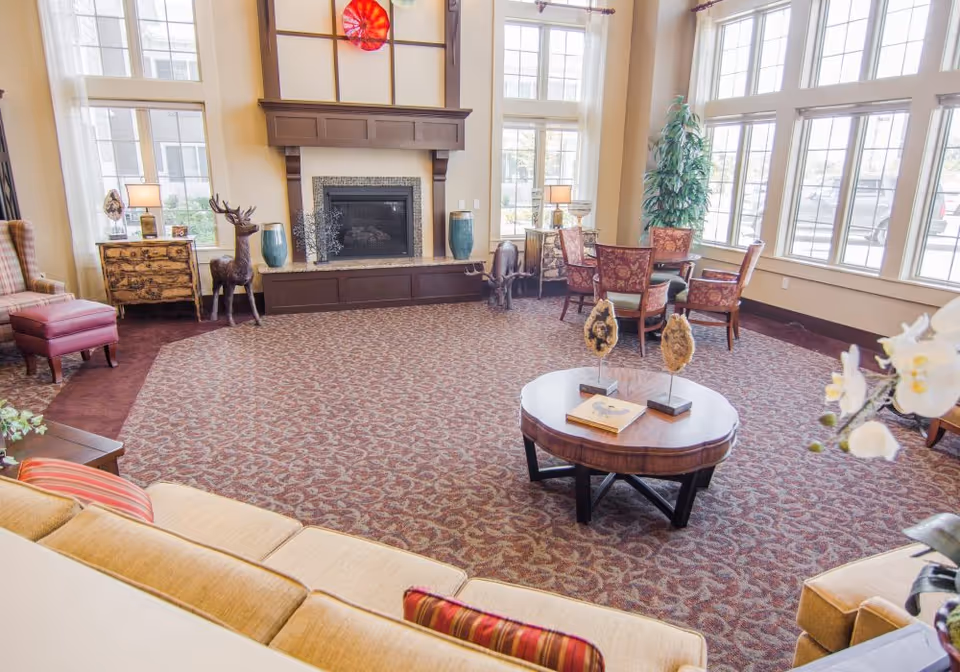 Bright, spacious lounge with sofas, armchairs, a round coffee table, fireplace, and large windows.
