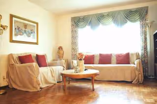 Cozy living room with beige sofas, red cushions, a wooden coffee table, and a large window.