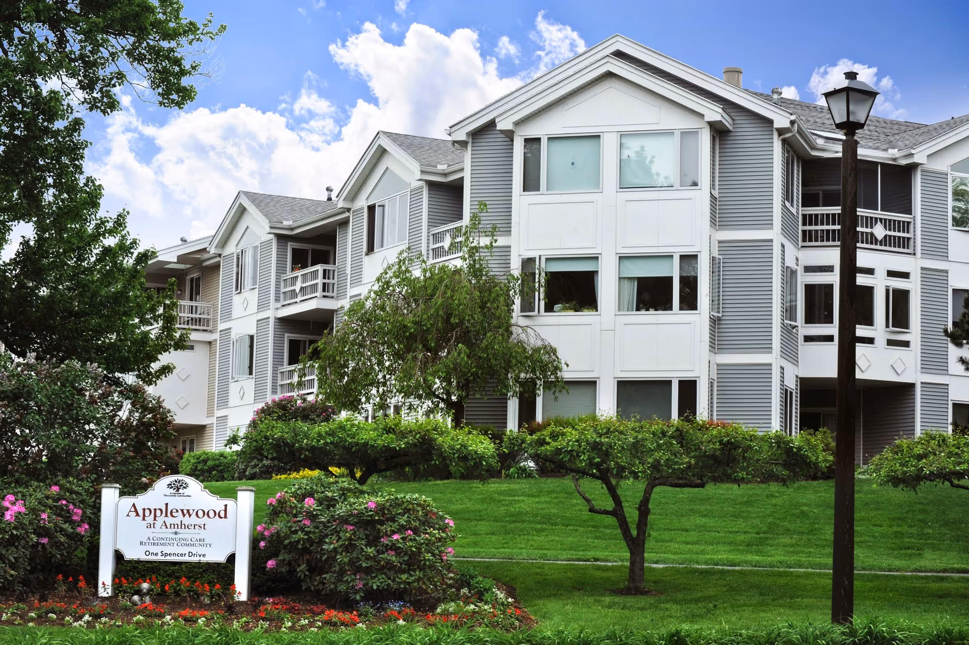 Exterior front of the Applewood at Amherst senior living building with lawns, shrubs, and a sign in the foreground.