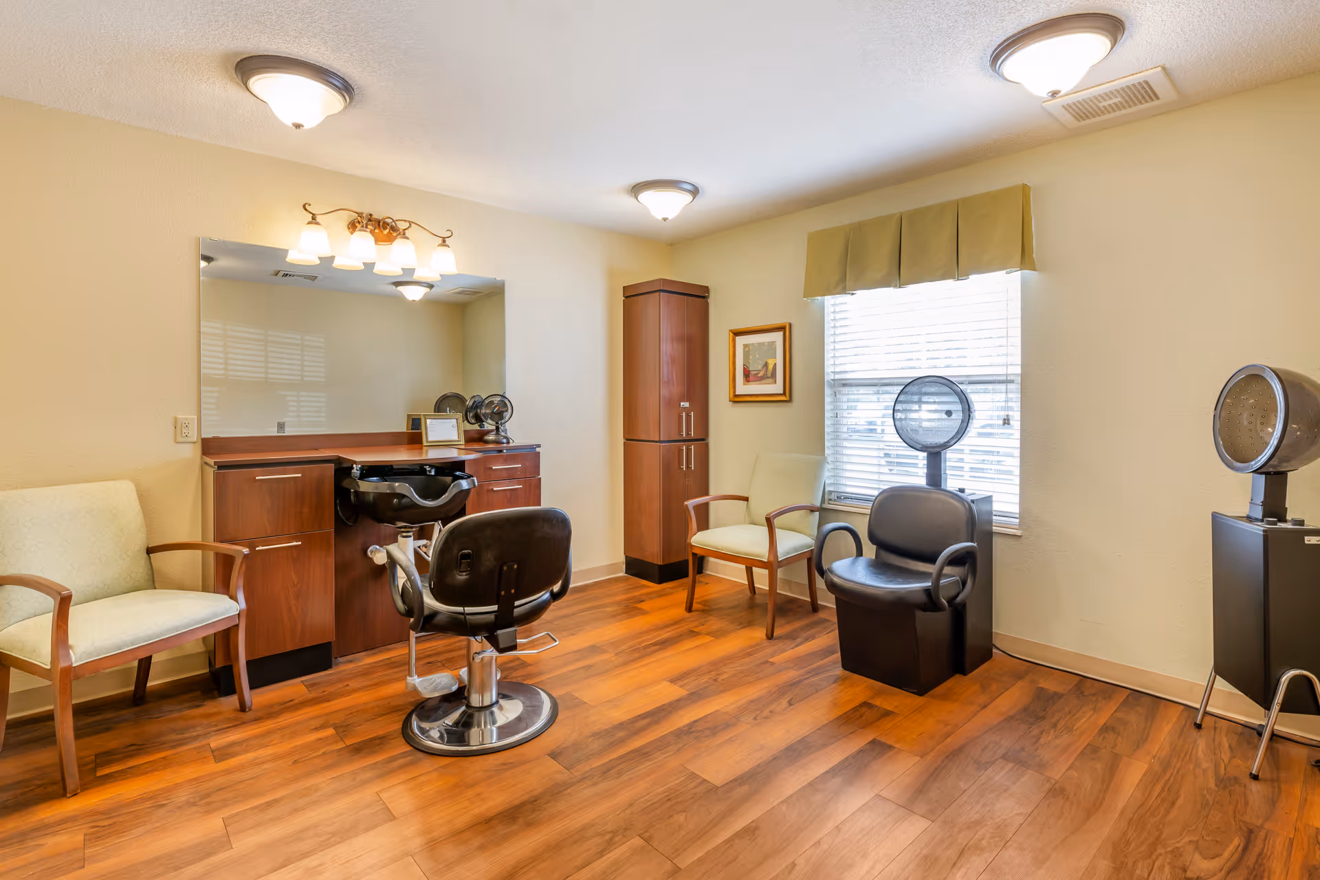 Bright interior salon room with styling chairs, hooded dryers, a large mirror, cabinetry and guest seating.