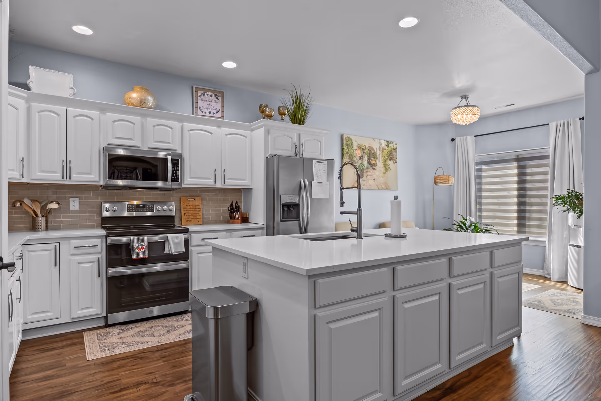 Bright modern kitchen with a large central island, white cabinets, stainless steel appliances, and an adjoining dining area.