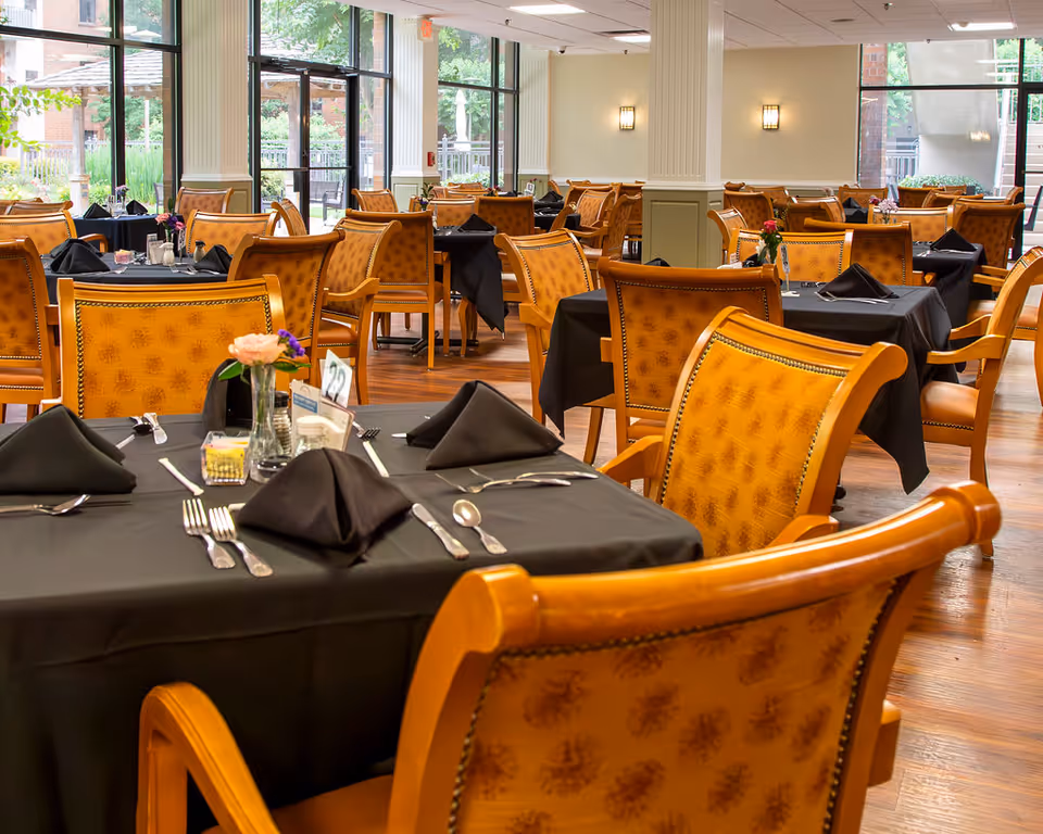 Spacious dining room with wooden chairs and tables set with black tablecloths and place settings.