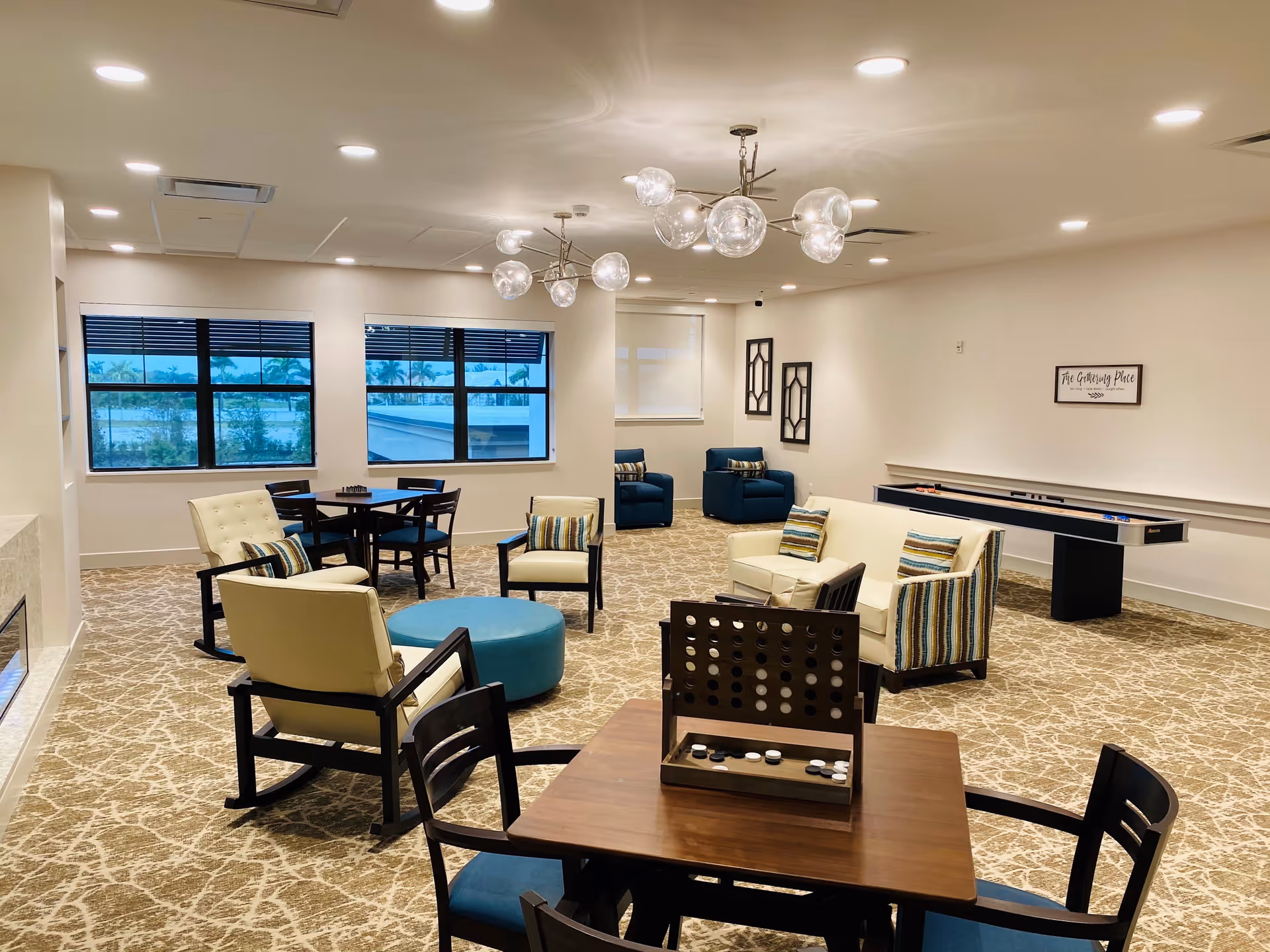 Bright communal lounge with multiple seating areas, game tables, and a shuffleboard table under modern lighting.