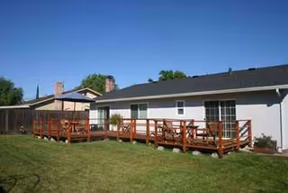 White single-story building with a long wooden deck and green lawn in backyard.