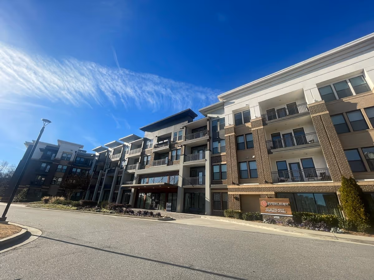 Multi-story senior living building with balconies and an entrance under a clear blue sky.