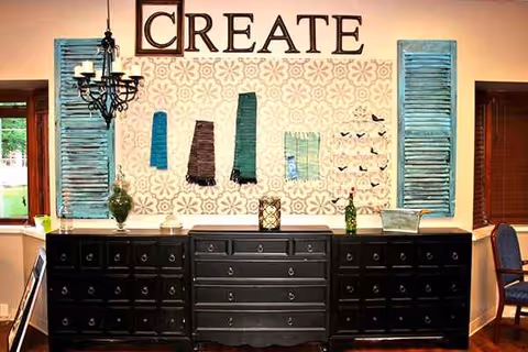 Interior craft room with a decorated wall labeled CREATE, blue shutters, and a black dresser.