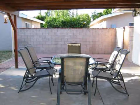 Outdoor covered patio with a central table surrounded by several patio chairs.