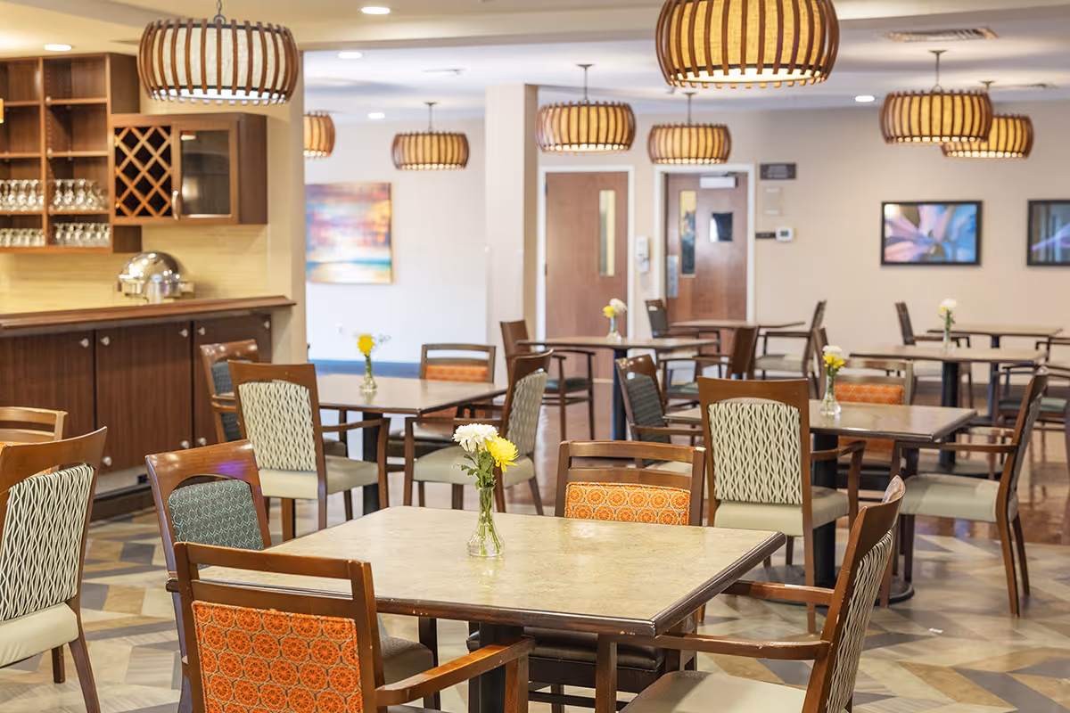 An indoor dining room at Coal Creek Post Acute & Assisted Living with several tables, chairs, and hanging pendant lights.
