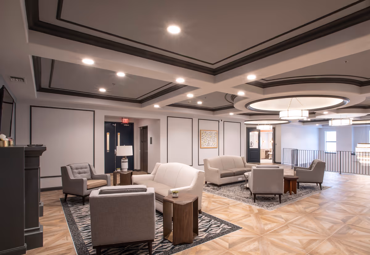 Spacious modern lounge with sofas, armchairs, side tables, patterned rugs, and recessed ceiling lights.