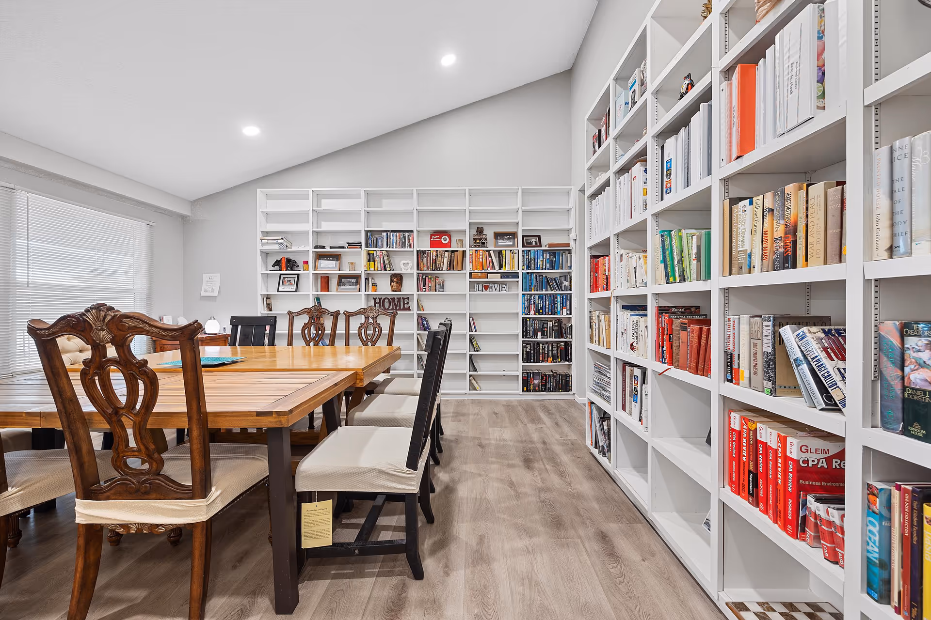 Spacious dining room with a long wooden table and chairs flanked by floor-to-ceiling white bookshelves filled with books.