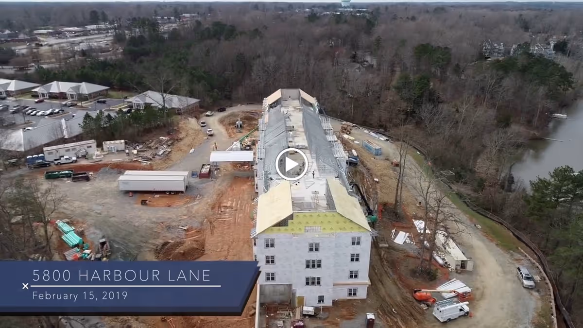Aerial view of a multi-story senior living building under construction surrounded by construction equipment, trees, and a nearby lake.