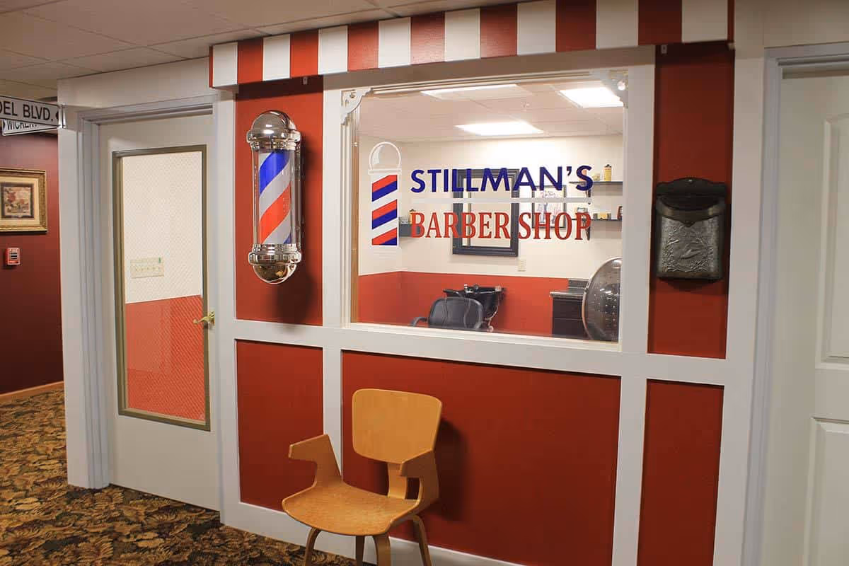 Interior hallway showing Stillman's Barber Shop window with a barber pole and a wooden chair outside.