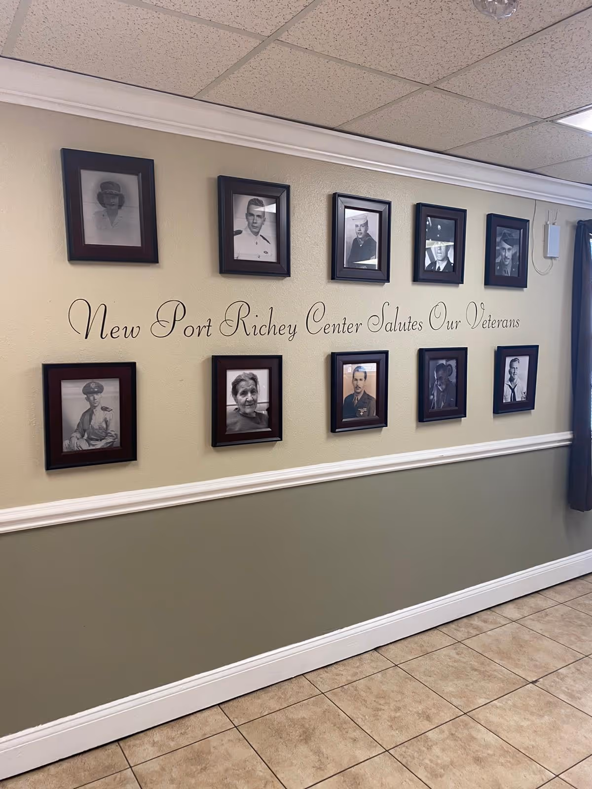 Hallway wall inside the facility with framed black-and-white portraits and the script 'New Port Richey Center Salutes Our Veterans'.