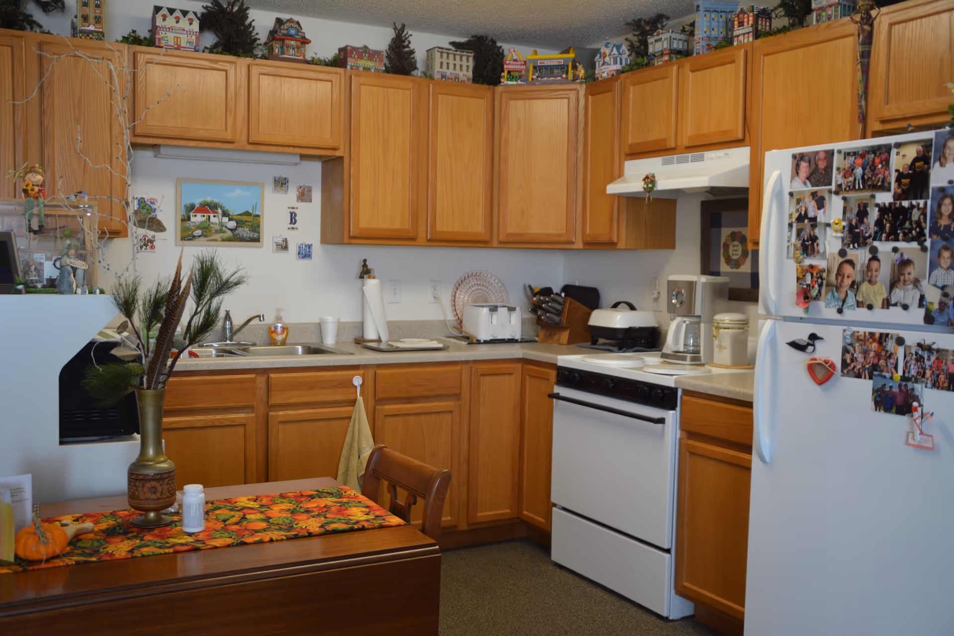 Small kitchen with oak cabinets, a white stove and refrigerator covered in family photos, a sink and countertop appliances.