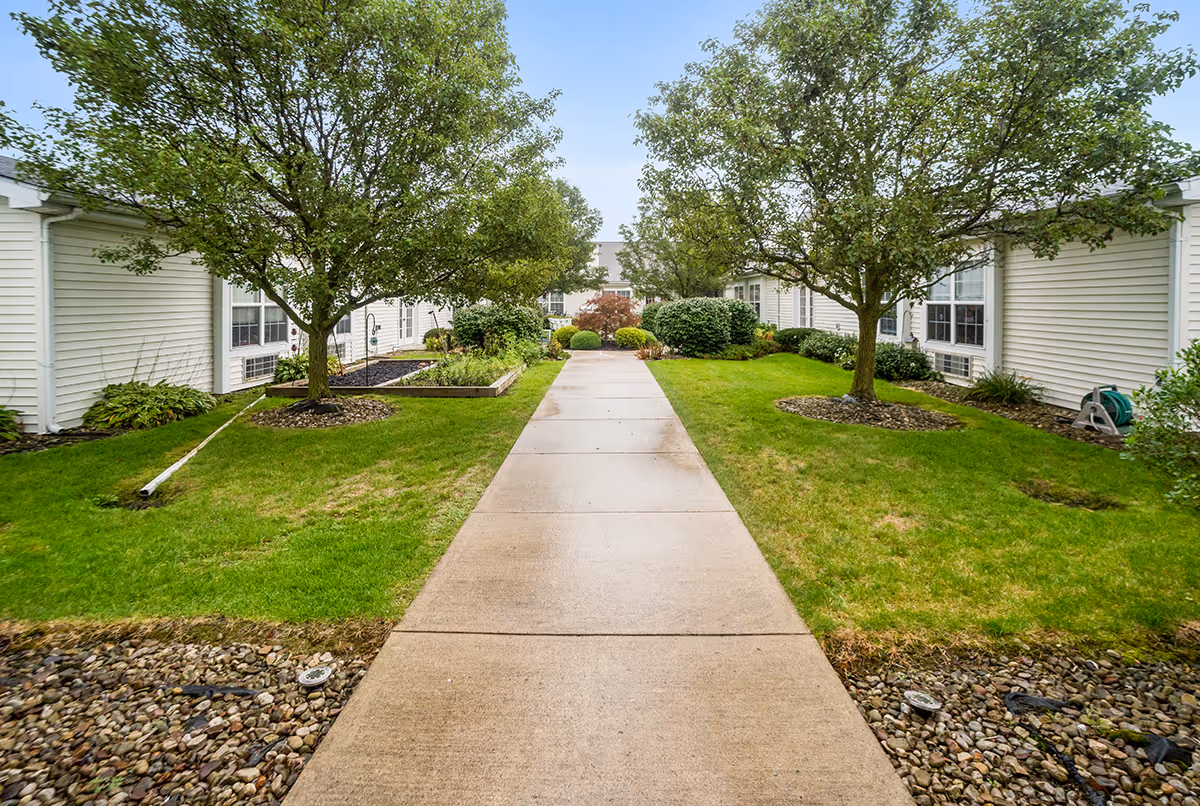 A concrete walkway leads through a landscaped courtyard with trees and lawns between single-story white buildings.