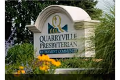 Stone sign for Quarryville Presbyterian Retirement Community surrounded by greenery and yellow flowers.