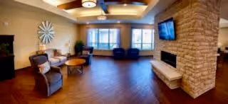 Spacious communal living room with seating, a stone fireplace and wall-mounted TV under large windows.