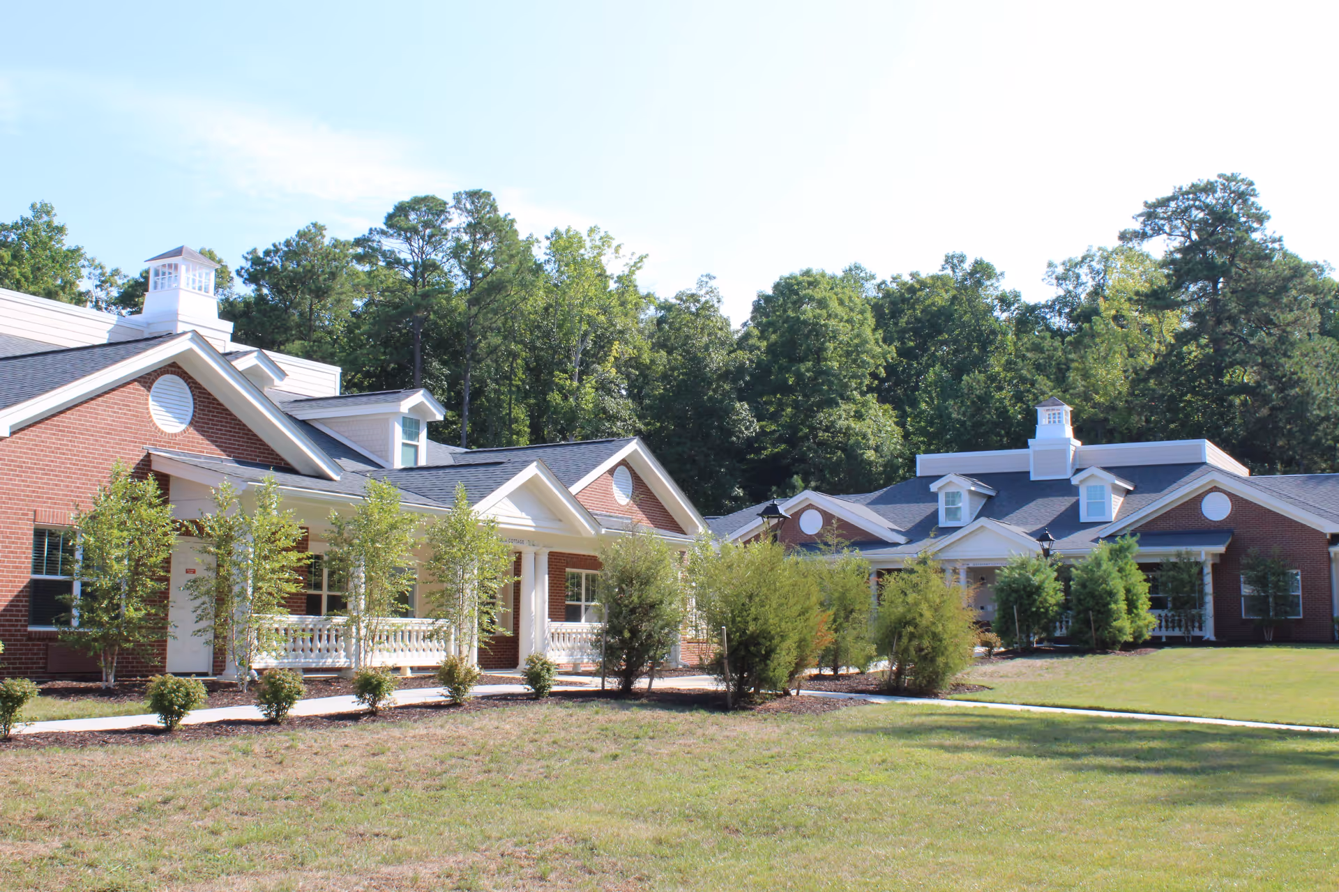 Front exterior of a single-story brick senior living building with gabled roofs, porches, and a landscaped lawn.
