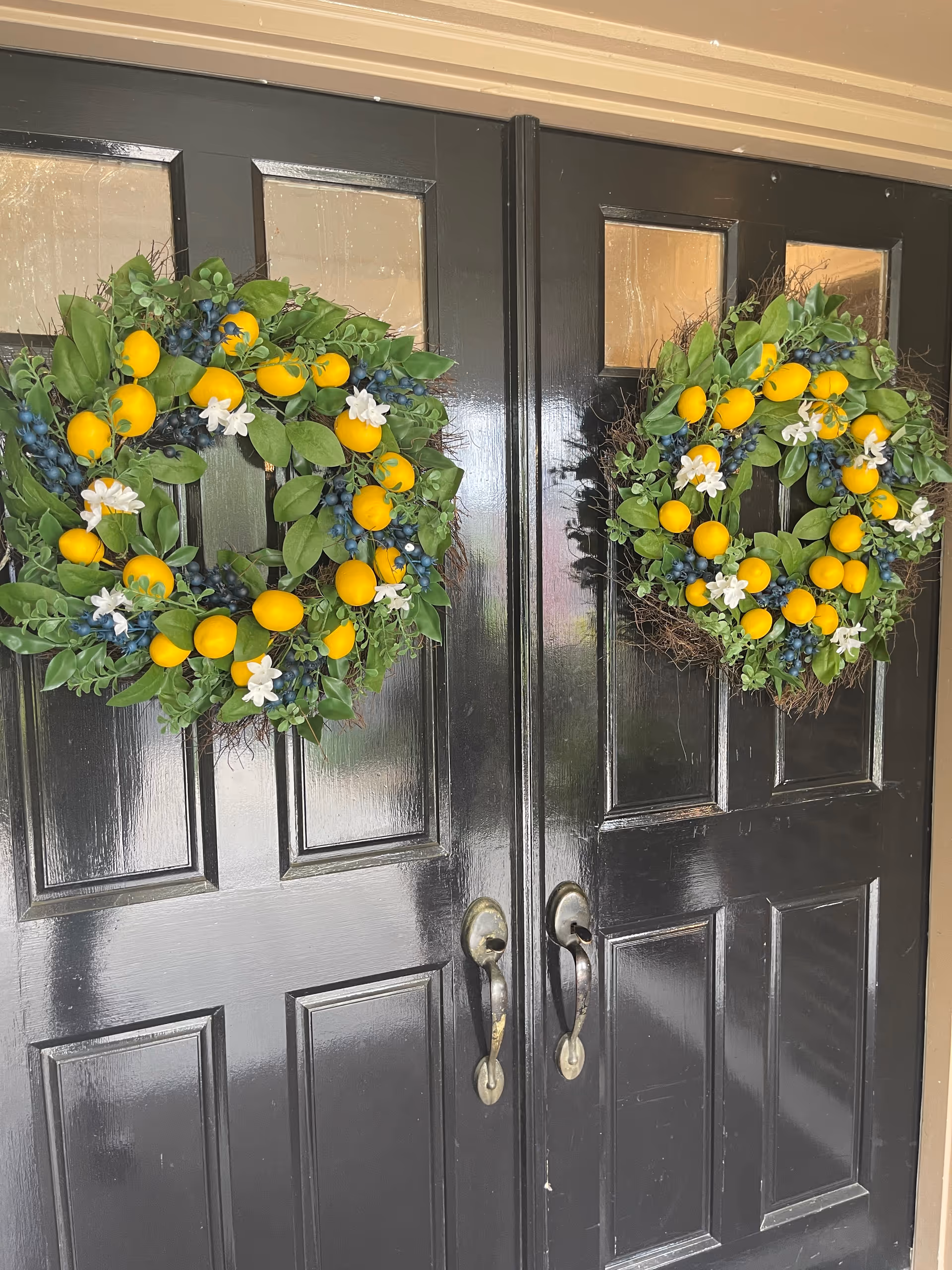 Double black front doors decorated with matching green wreaths of yellow lemons and blue berries.