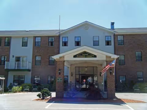 Two-story brick-and-white senior living building with a covered entrance and American flag.