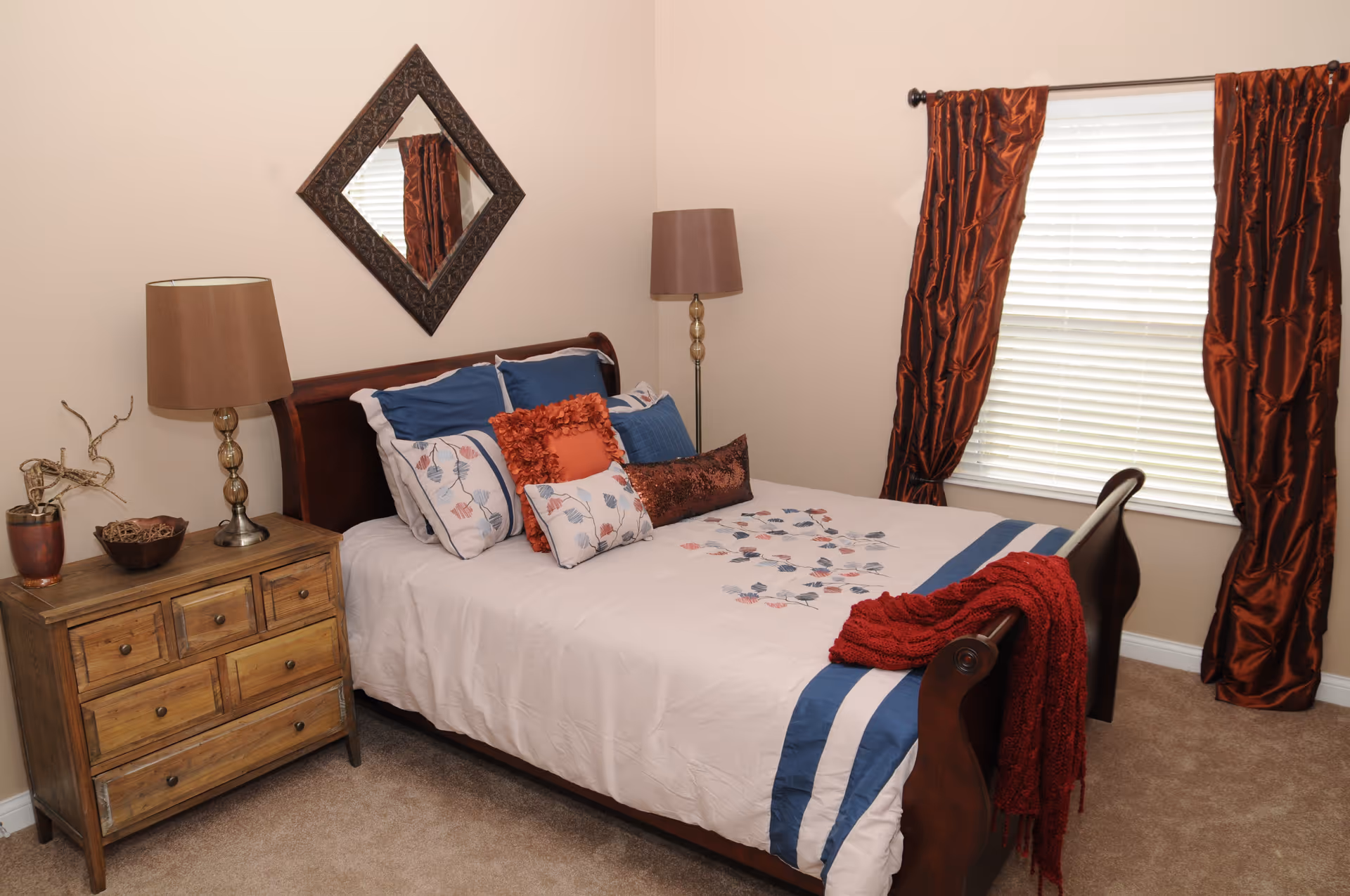 Cozy bedroom in a senior living facility with a bed, nightstands, lamps, and curtains.