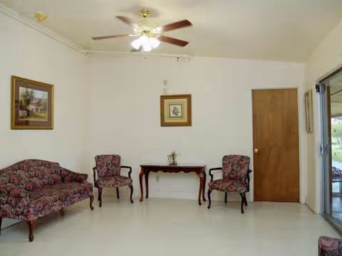 A spacious living room with floral seating, a wooden console table, ceiling fan, and wall art.