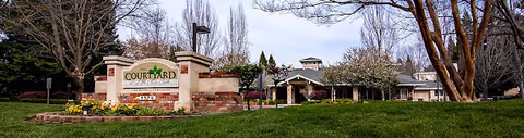 Front entrance sign and landscaped lawn of Courtyard At Little Chico Creek with the single-story facility building and trees behind it.