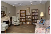 Cozy living room with bookshelves filled with media, an upholstered sofa and armchairs, a floor lamp, and framed artwork.
