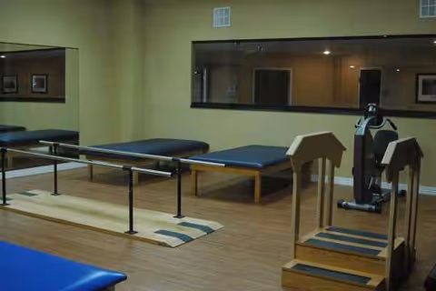 Indoor rehabilitation room with parallel bars, mats, and exercise equipment.