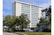 Exterior view of a multi-story white residential building with trees and parked cars in front.