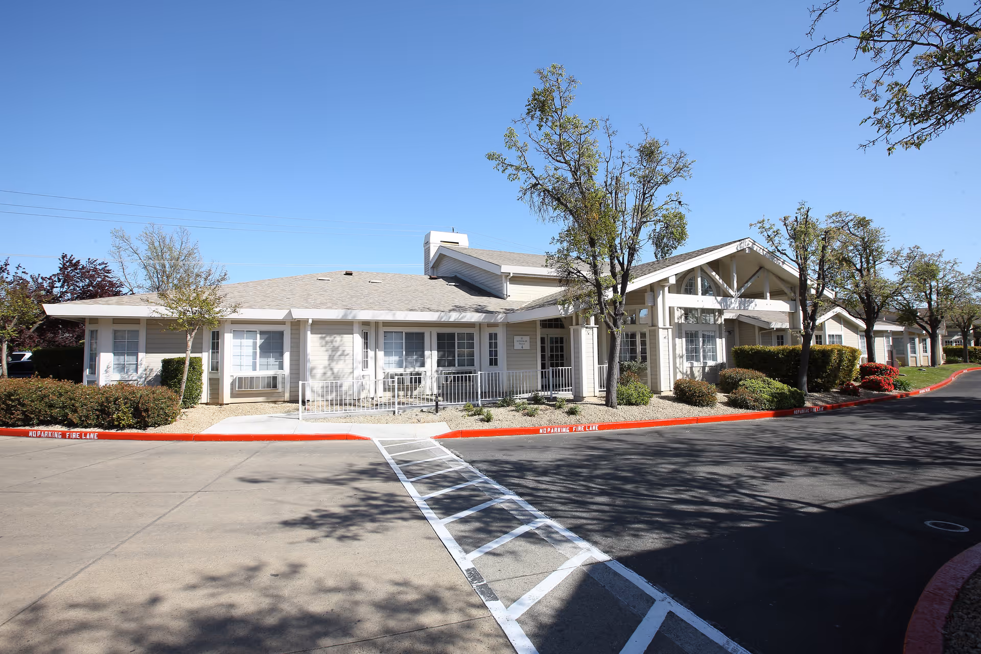 Front exterior of a single-story senior living facility with a covered entrance, landscaping, and a driveway.