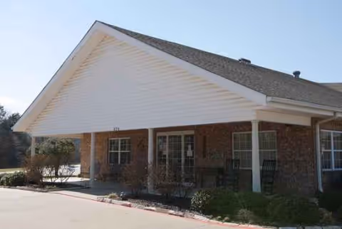 Brick senior living facility entrance with a covered porch, columns, and front-facing windows.