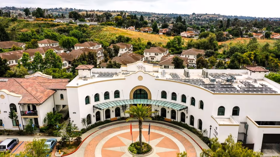 Aerial view of the white Mediterranean-style Oceanside Senior Living building with a circular entrance driveway and surrounding residential neighborhood.