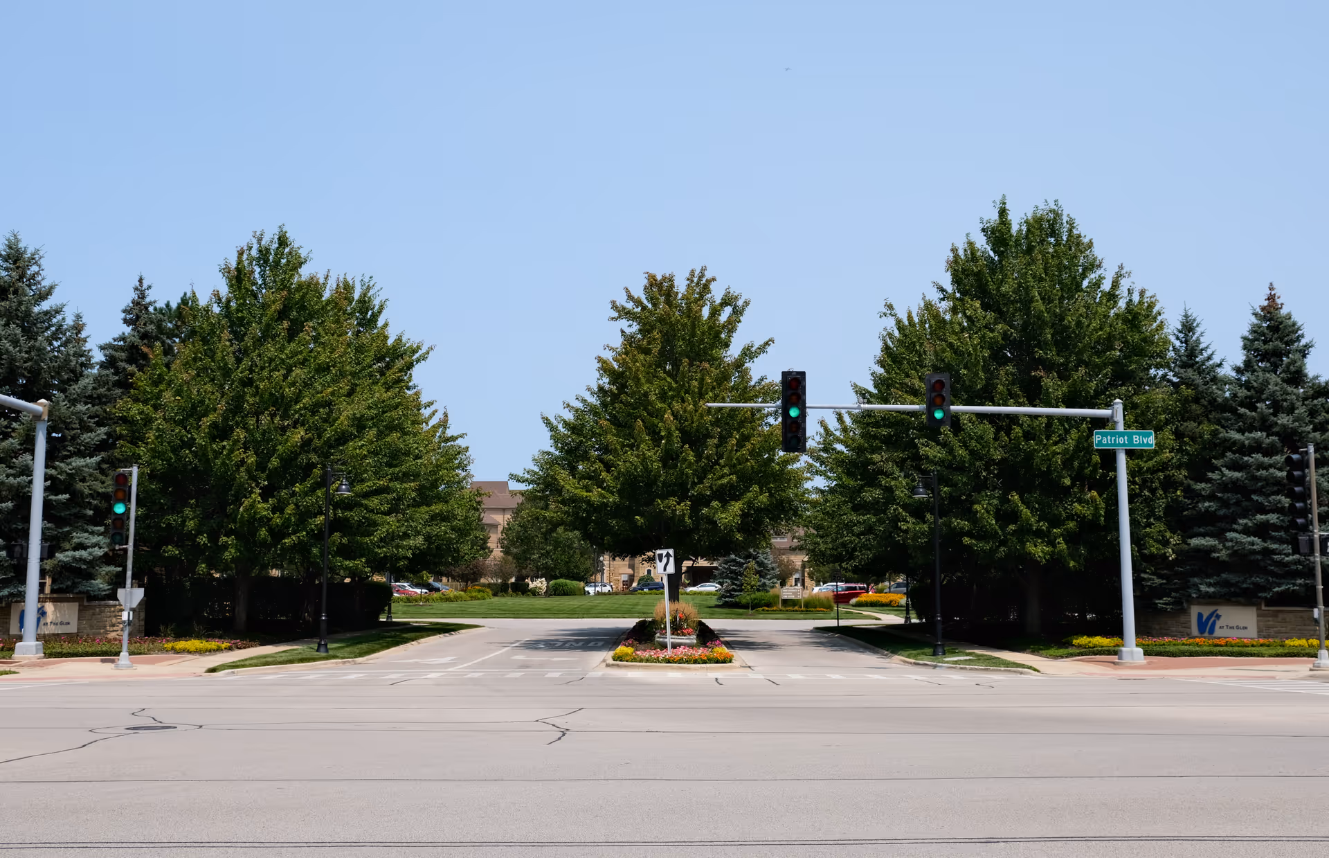 Street view of a tree-lined entrance with traffic lights and a landscaped median leading to a senior living facility.