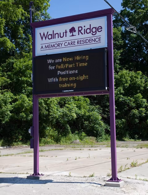 A hiring sign at Walnut Ridge, displaying job openings for full and part-time positions with details about free on-site training, surrounded by greenery.