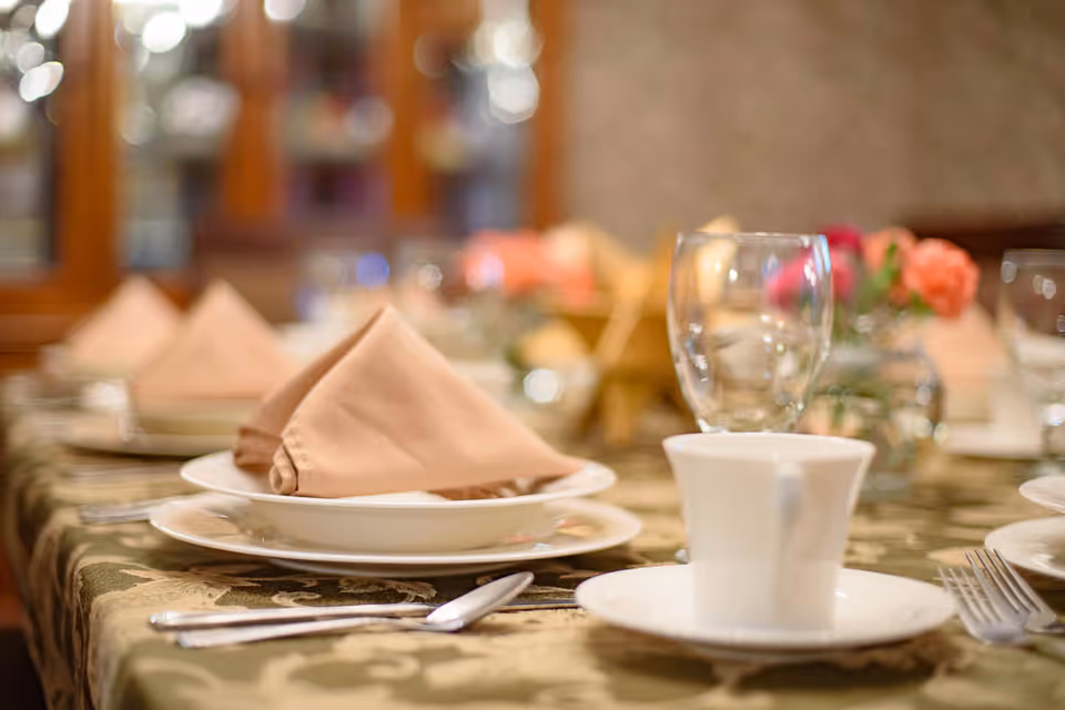 Close-up of a formally set dining table with plates, folded cloth napkins, glassware, and a coffee cup.