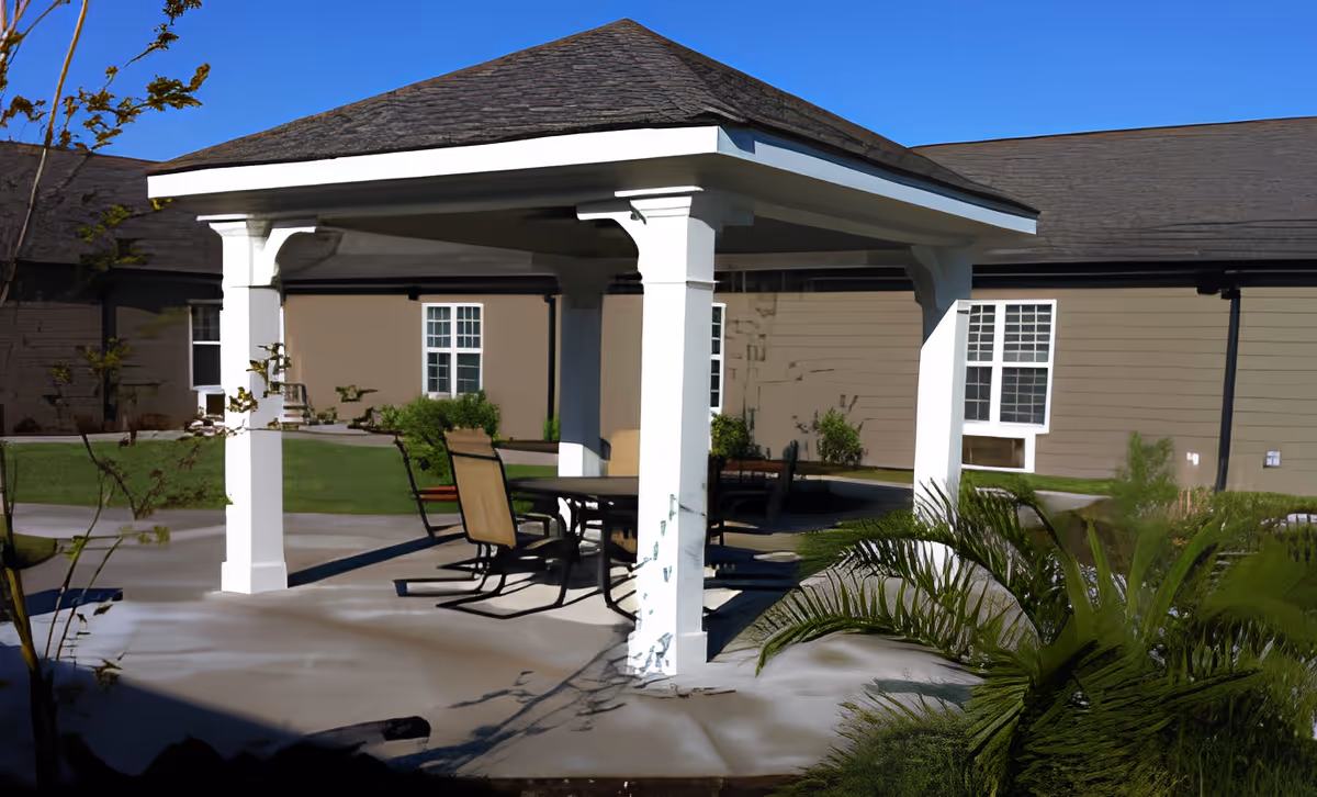 A white-roofed outdoor pavilion with a table and chairs on a concrete patio in the courtyard of a single-story residence.