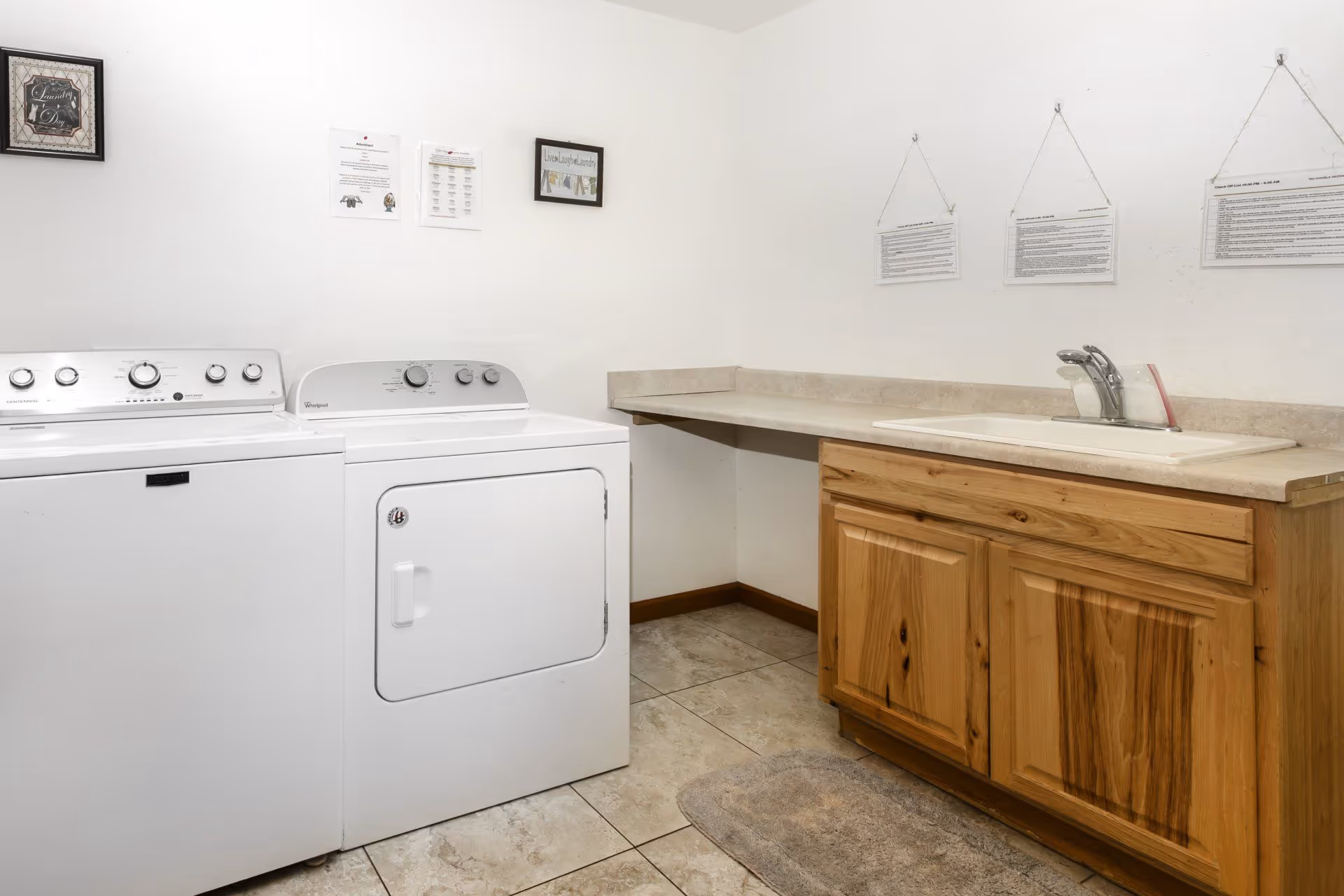 Laundry room with a washer and dryer, a countertop with sink and wooden cabinet, and tiled floor.