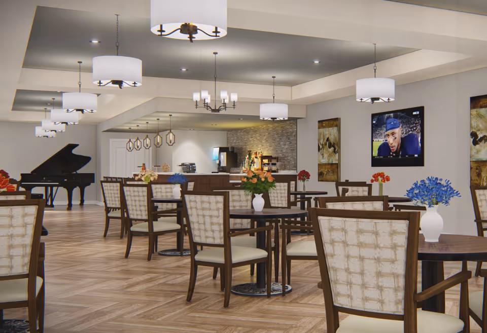 A spacious dining room with multiple round tables and cushioned chairs. Each table has a vase with colorful flowers. The room features modern pendant lights hanging from the ceiling, a grand piano in the corner, and a wall-mounted TV displaying a sports game. The back of the room has a counter area with coffee machines and a textured stone wall.