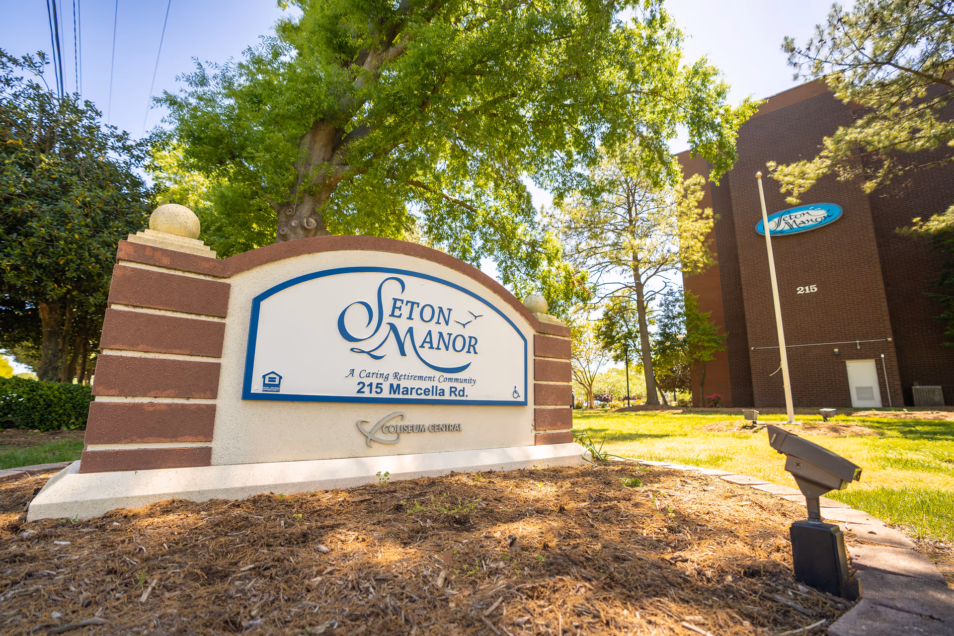 Entrance sign reading "Seton Manor" in front of a brick building and trees on a sunny day.
